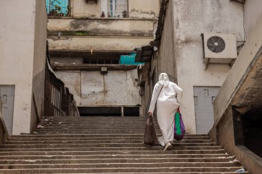 Arab or muslim woman is walking up a long set of stairs in dirty environment. Typical view of a city in Oran, Algeria. Frequently used stairs but neglected, covered in filth clipart