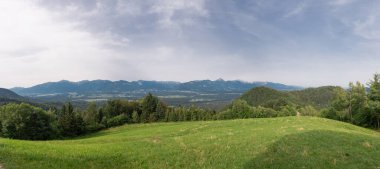 Wide panorama of the karawanken alps from the magical Jamnik church above Kropa in Slovenia. Blue sky and green meadows and forests in front of picturesque mountains clipart