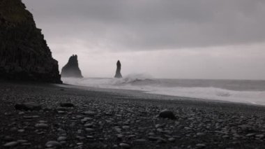 İzlanda 'da Reynisfjara sahilindeki dalgaların manzarası. Büyük bazalt sütunlar sudan ve kayalık plajlardan tırmanıyor. Kumsalda soğuk rüzgarlı bir yer Büyük dalgalarla.