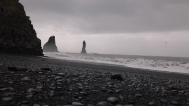 İzlanda 'da Reynisfjara sahilindeki dalgaların manzarası. Büyük bazalt sütunlar sudan ve kayalık plajlardan tırmanıyor. Kumsalda soğuk rüzgarlı bir yer Büyük dalgalarla.