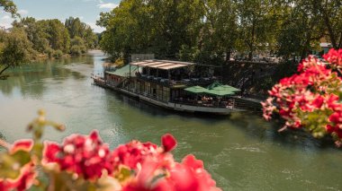 Banja Luka 'nın merkezindeki Vrbas nehrine demirlemiş bir sal veya tekne, restoran olarak kullanılıyor. Köprüden bazı çiçeklerin arasından bak.