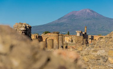 Pompei arkeolojik alanındaki harabelerin genel görünümü, yakın arkaplanda görkemli Vesuvius dağı olan görünür sütunlar ve duvarlar