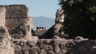 Pompei arkeolojik alanındaki harabelerin yavaş çekim görüntüsü, görünür sütunlar ve yakın arkaplanda görkemli Vezüv Dağı olan duvarlar..