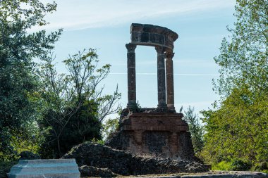 Pompei 'nin antik bölgesinde bir duvar veya evin kalıntıları. Görünür üç sütun yeşillikler arasında, mavi gökyüzü arka planda..