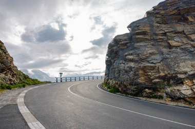 İki taş ya da kaya duvarının arasına oyulmuş, dağ geçidinde güzel bir asfalt olan güzel bir yol kıvrımı. Arkasında güneş olan güzel bulutlar.