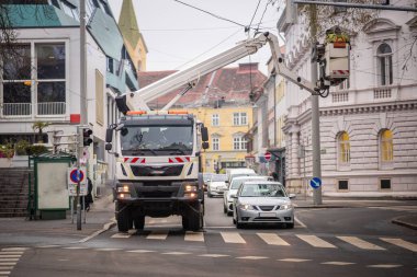 Sokakta sepeti olan bir kamyon sokak lambaları için kablo onarıyor ya da otobüs için kateneri. Caddenin yukarısında beyaz bir kamyonet var..