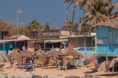 Beach bar and small port with houses at Almadies, the most western part of mainland africa. People relaxing under the thatched roof clipart