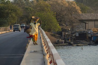 Rear view of a typical african woman walking with basked on head over the bridge over Casamance river in Zuiguinchor, Senegal. Typical african feeling. clipart