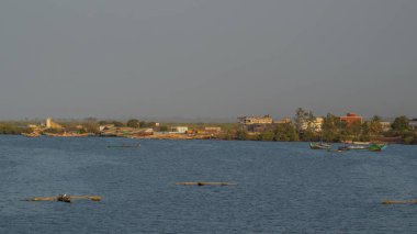 Evening hours or sunset in ziguinchor, coastal city in southern senegal. Visible docks and some houses. Blue hazy sky. clipart