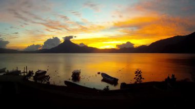 Akşam Guatemala 'daki Atitlan Gölü' nün panoramik manzarasında gün batımının zengin çiçekleri ve ön planda bazı tekneler..