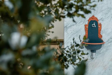 Mermer bir duvara monte edilmiş eski bir süs su havzası ve musluğun ön manzarası. Yan taraftaki altın süsler..