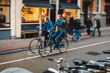 Amsterdam, Hollanda, 1.11.2013: Bisikletli genç bir çift bisiklet yolunda koşuyor, etraflarında hareket bulanıklığı var.