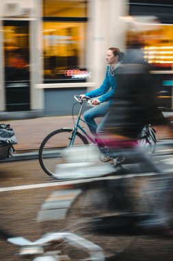 Amsterdam, Hollanda, 1.11.2013: Bisikletli bir kadın bisiklet yolunda koşuyor, etrafında hareket bulanıklığı var.