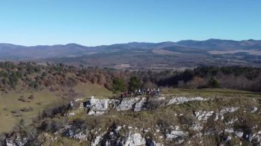 Pivka ya da Narin etrafındaki bir uçurumun kenarında yürüyen yürüyüşçüler Pivka, Slovenia 'ya yakın kahverengi sonbahar manzarası. Yürüyüşçülerin güneşin altında dolaşmalarını gösteren drone görüntüsü.