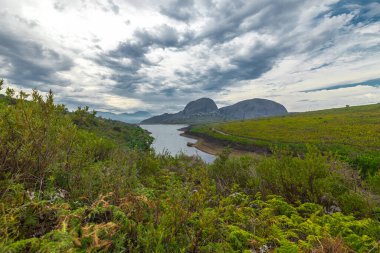 Güney Afrika 'daki Paarl şehrinin üzerindeki Paarl Dağı Doğa Koruma Alanı panoraması. Görünür göl ve büyük yuvarlak granit kaya oluşumlarının hakim olduğu fynbos bitki örtüsüyle bulutlu bir gün..