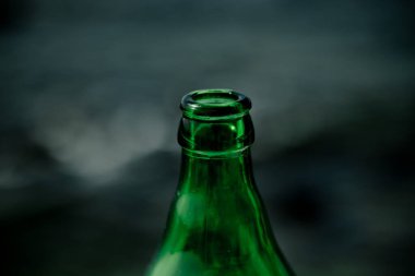 Yakından çekilmiş yeşil cam bir şişe boyun ve kapak, bulanık bir arka plan üzerine kurulmuş. Odak, şişe dokusunu ve rengini vurguluyor, minimalist ve sanatsal bir kompozisyon oluşturuyor