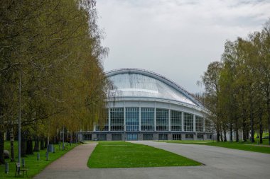 Tallinn 'deki Klaassaal arenası, eğri dizaynlı, büyük cam pencereli ve önde gelen bir kulesi olan modern bir yapı. Etrafı yemyeşil çimlerle ve bulutlu bir gökyüzünün altında yapraksız ağaçlarla çevrili. Yol ışıklarıyla kaplı.