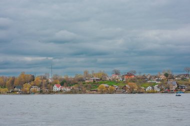 Narva, Estonya 'dan sakin bir nehir boyunca Rusya' ya doğru bakan sakin bir manzara. Renkli evleri, yemyeşil yeşillikleri ve sudaki küçük teknesi olan bulutlu bir kıyı şeridi üzerine çöker. Manzara huzurlu bir sınır manzarası yakalıyor.