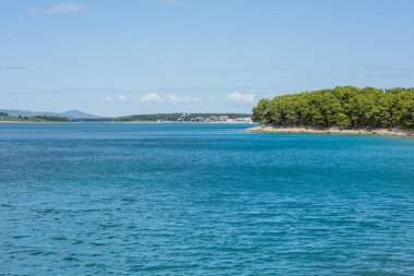 Draga Körfezi 'nden nefes kesici bir manzara, kristal berrak suların çam ağaçlarıyla çevrili uzak bir kıyı şeridiyle buluştuğu Pakostan' a bakıyor. Sakin deniz manzarası engin, parçalı bulutlu bir gökyüzünün altında parlar. Mükemmel bir doğal geri çekilme..