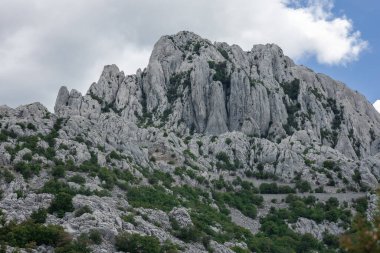 Velebit 'teki Tulove Grede' in engebeli zirveleri görkemli bir şekilde yükselir. Keskin kireçtaşı kayalıkları ve yemyeşil alanları parçalı bulutlu gökyüzü tarafından çerçevelenir..