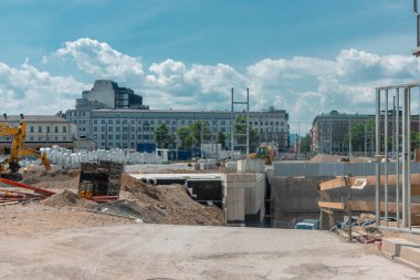 2025 yılının parlak bir Temmuz gününde Ljubljana Tren İstasyonu 'nda inşaat gelişir. Kazıcılar kazıyor, beton yükseliyor ve şehir manzarası gelişim süreciyle gelişiyor. Gökyüzü kabarık bulutlarla berrak, kentsel yenilenmeyi doğayla harmanlıyor..