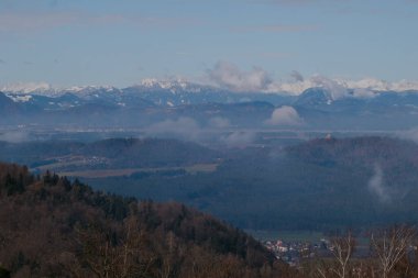 Görkemli Kamnik Alpleri, Slovenya 'nın Ljubljana kenti yakınlarındaki sisli bir vadiden yükseliyor. Sabahın erken saatlerinde parlayan engebeli tepeler ve karlı zirvelerle.