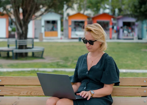Image of happy woman using laptop while sitting in park.  Young woman working on laptop.