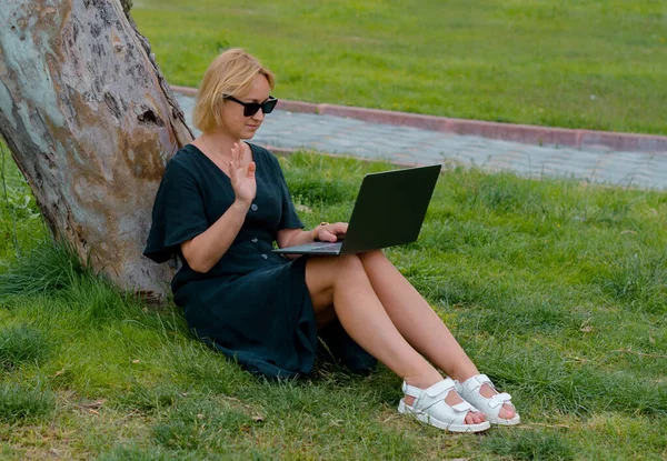 Image of happy woman using laptop while sitting in park. Young woman working on laptop.