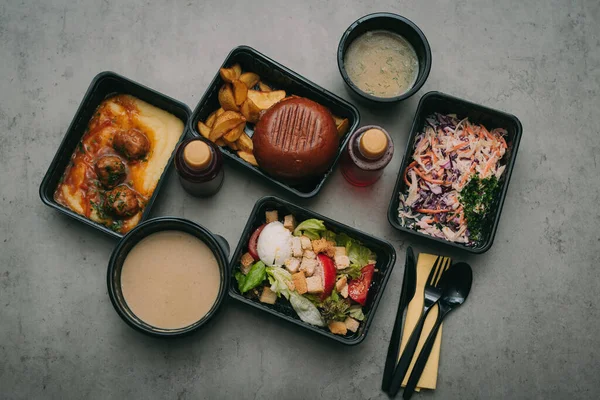 Containers with tasty takeout meals on dark background, top view. Food delivery