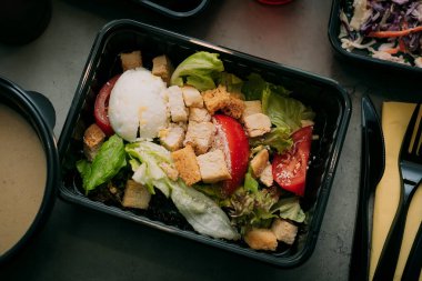 Ready healthy food catering menu in lunch boxes fish and vegetable packages as daily meal diet plan courier delivery with fork isolated on black table background. Take away containers order concept.