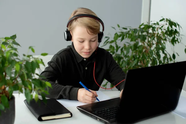 Teenage boy wearing headphones works at desk in his bedroom