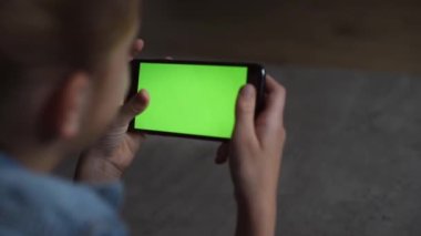 4k Over the shoulder view of a blank mobile phone screen held by teenage girl relaxing at home holding it in the horizontal position