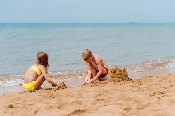 Erkek ve kız sahilde yaz tatillerini üzerinde oynama. Denizde bir sandcastle bina çocuk