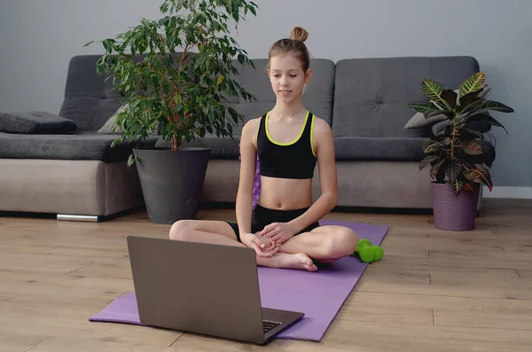 young girl in sportswear watching online video on laptop and doing fitness exercises at home. Distant training with personal trainer, social distance, online education concept