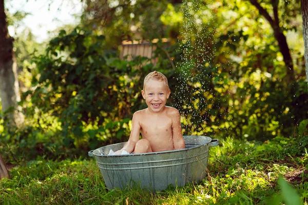 stock image Summer vacation in countryside, local staycation. Cute boy having fun, bathing and splashing in old iron bowl on the backyard , happy summertime, outdoor lifestyle