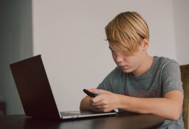 Genç çocuk bilgisayar ve akıllı telefon kullanarak öğrenim görüyor.