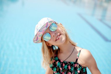 Güneşli bir günde, güneş gözlükleriyle havuzda gülümseyen tatlı kız.