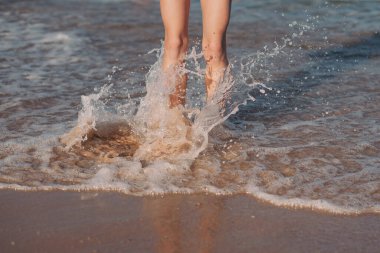 Dişi ayaklar deniz dalgasına basıyor. Yaz tatilleri konsepti