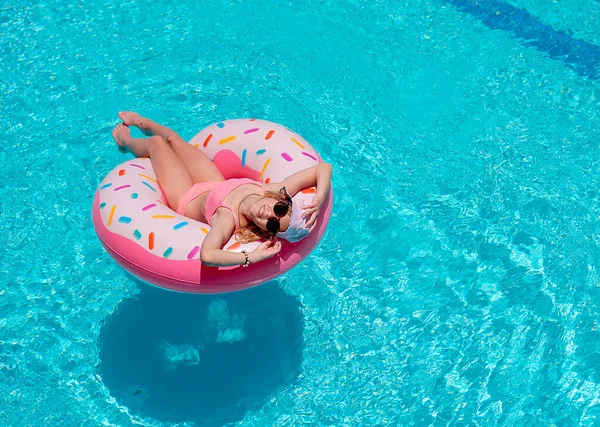 young girl in a bathing suit relaxing on inflatable rubber ring in swimming pool. Enjoying summer. Vacation mood