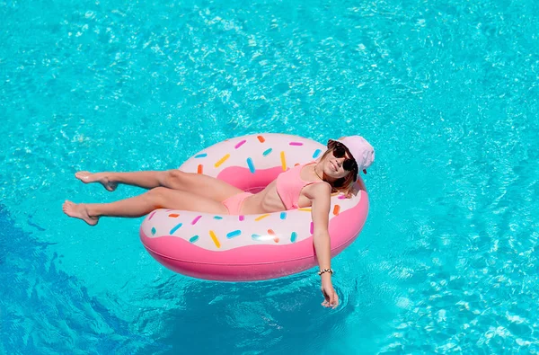 Bikinili genç bir kız, yüzme havuzunda şişme bir şapkayla rahatlıyor. Lüks tatil köyünde güneşlenen kız.