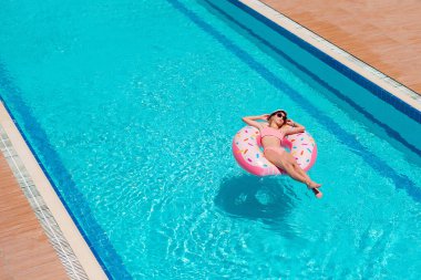 Havuzda yüzen güzel bir kızın havadan görünüşü, rahatlamak şişme yüzükle yüzmek ve aile tatilinde suda eğlenmek.