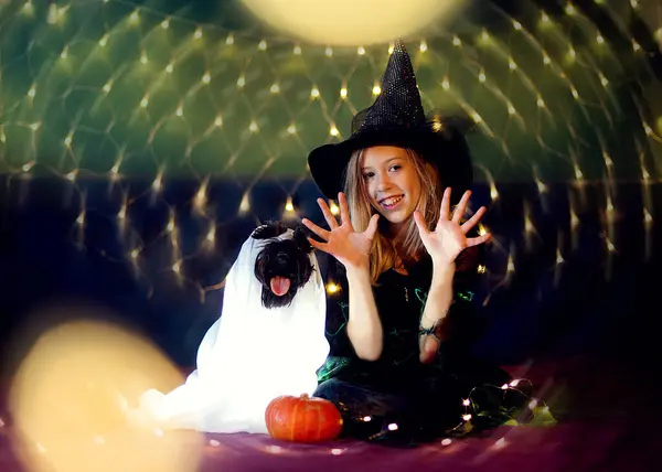 Cadılar Bayramı kostümlü komik kız çocuğu ve Drakula pelerinli balkabaklarıyla süslenmiş siyah şapka.