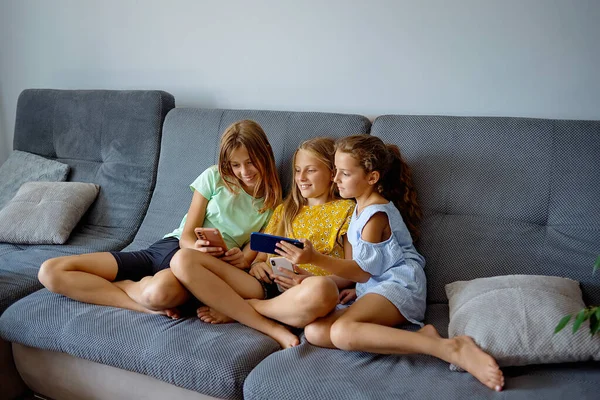 girls playing mobile game on smartphone sitting on a sofa. Child leisure at home, video gaming addiction
