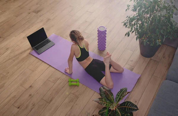 girl doing sports at home, sitting on yoga mat in bright room at home, workout indoors. Sport and wellbeing