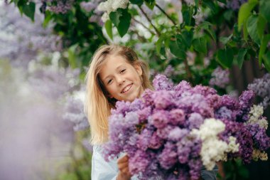 Bir buket leylakla güzel bir genç kız, leylak içinde bir kız, baharda leylaklar. Genç kız bir demet leylakla poz veriyor.