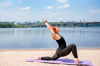 Genç fitness kadını dışarıda spor yapıyor. Nehrin kenarında geriniyor.