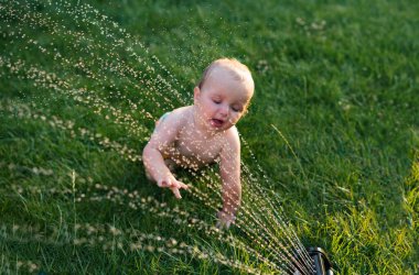 Mutlu çocuklar su sıçratır ve bahçe hortumuyla oynar. Sıcakta su sıçratmayı sever. Çocuklar için yaz eğlencesi ve açık hava eğlencesi.