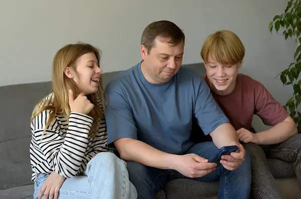 Stock image happy family with kids watching funny video on phone sitting on couch enjoy weekend at home, modern tech leisure activities free time concept