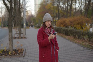 Sonbaharda sokakta yürürken ve mesajlaşırken giyilen akıllı telefon.