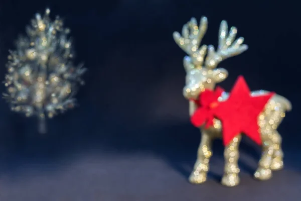Bokeh Noel geçmişi. Koyu arkaplanda Noel ağacı olan altın renkli, parlak ren geyiği heykelciği. Noel arkaplanı / kartı, hediye kartı, kırmızı yıldız - kolye / etiket. Kopya alanı olan Noel duvar kâğıdı.